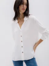 Camisa blanca de manga larga con cuello clásico, cierre de botones y corte holgado.