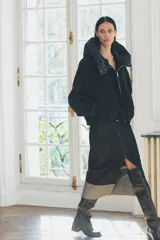 Chaqueta negra de cuello redondo confeccionada en hilatura con 50% lana. Tiene capucha extraíble, manga larga con puño interior, bolsillos delanteros y bajo ajustable con cordón elástico. Cierre frontal con cremallera metálica.