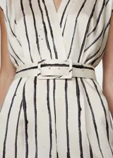 Mono largo de tejido satinado color crudo con rayas verticales negras. Tiene escote cruzado en V, sin mangas, cinturón desmontable con hebilla cuadrada y cierre trasero invisible.