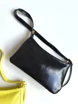 Cartera baguette de cuero sintético color amarillo pastel, con correa de hombro del mismo material y cierre superior.