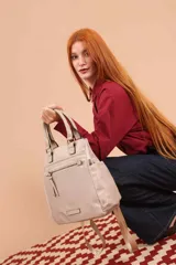 Mochila bandolera color marrón con herrajes color peltre. Tiene un compartimento principal amplio con cierre, un bolsillo frontal con cierre y dos bolsillos laterales abiertos. Incluye correa ajustable para usar al hombro o cruzada.