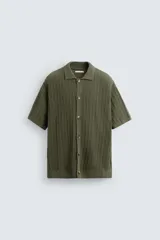 Camisa de hombre color verde militar, de punto con estructura abierta, corte regular fit, cuello solapa, manga corta y cierre frontal con botones.