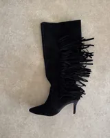 Bota alta de cuero vacuno color negro, con punta fina, taco aguja y detalle de flecos en el lateral externo.