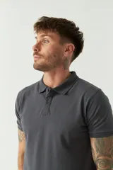 Remera polo negra de manga corta con cuello clásico, cierre de botones, bolsillo en el pecho y logo estampado.