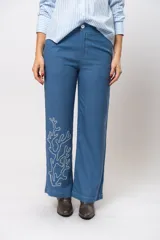 Conjunto de camisa de manga corta con cuello y pantalón de corte recto, ambos de tela simil lino color beige con bordados blancos.