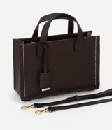 Cartera tipo satchel estructurada de color marrón oscuro, con costuras decorativas en contraste color crema en los laterales. Posee asas superiores cortas y una correa larga ajustable y desmontable. Los herrajes son de color dorado.