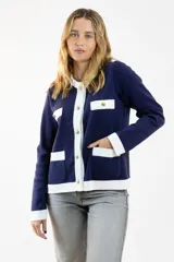 Chaqueta azul marino tejida en lana con ribetes blancos, cuello redondo, cierre frontal con botones dorados y bolsillos frontales con solapa blanca.