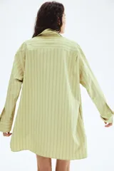 Vestido camisero de manga larga, color verde claro con finas rayas verticales oscuras. Presenta cuello de pico, botonadura frontal y corte evasé/oversized.