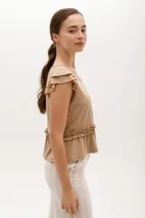 Remera color beige con cuello redondo, mangas cortas con volados y frunce con volados en la cintura.