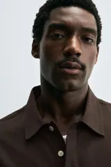 Camisa tipo polo de corte relajado confeccionada en una mezcla de lyocell y algodón. Presenta cuello con solapa, cierre frontal de botones ocultos, manga corta y un bolsillo de parche en el pecho. El bajo cuenta con aberturas laterales.