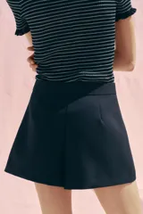 Falda pantalón corta color azul marino, de tiro alto y corte recto. Presenta doble hilera de botones blancos en el frente y cierre lateral con cremallera oculta.