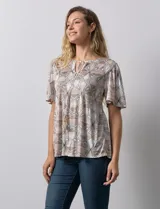 Blusa de tejido elastizado con estampado geométrico en tonos beige y blanco. Tiene cuello redondo con escote en V y lazo de ajuste, y mangas cortas amplias. Marca Cupio.