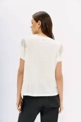 Remera blanca de lino con mangas cortas y calce al cuerpo. Presenta cadenas de strass en los hombros.