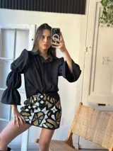 Camisa negra con cuello clásico, mangas largas abullonadas con puños elásticos y cierre frontal con botones.