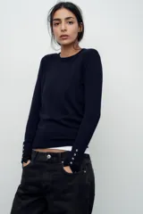 Sweater negro de punto liso con cuello redondo y mangas largas con botones dorados en los puños.