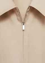 Mono color beige de lyocell y lino, con cuello camisero, manga corta, cierre frontal con cremallera, lazo ajustable en la cintura, bolsillos laterales y corte recto.