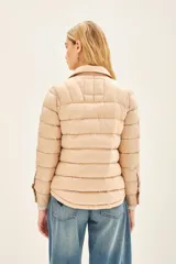 Campera puffer color beige con cuello camisero, cierre con botones a presión, bolsillos con solapa en el pecho y relleno de plumas.