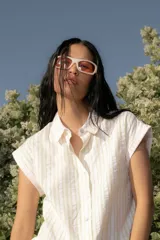 Vestido corto tipo camisero confeccionado en algodón a rayas finas en tonos neutros, de silueta amplia y falda con volados. Diseño abotonado y cuello clásico.