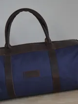 Bolso de lona color negro con detalles en cuero color tostado. Tiene doble asa de mano y correa de hombro ajustable y extraíble.