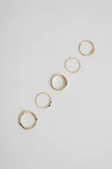 Set de cinco anillos dorados con diferentes diseños: uno con bolitas, uno con forma de olas, uno con textura trenzada, uno con una circonita y uno liso con forma curva.