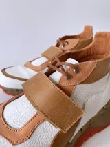 Zapatillas deportivas blancas con detalles en cuero color salmón y suela gruesa con detalles en naranja.