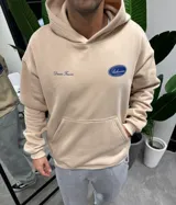 Canguro beige de algodón con capucha y estampado en la espalda con el texto "BRITISH SPORTSWEAR Bohemian COMPANY Dream Forever" en color azul.