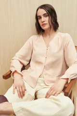 Camisa marrón de manga larga con escote en V y botones forrados al tono en el frente. Destaca por su textura sutil y por el detalle de frunces con volados en la parte inferior.