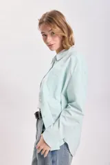 Camisa de manga larga con cuello clásico, corte recto y cierre frontal con botones. Diseño a rayas verticales finas en color verde agua y blanco.