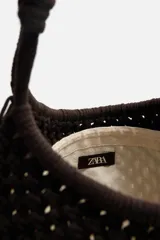 Bolso tipo shopper color marrón oscuro, confeccionado en tejido trenzado de algodón con diseño de macramé. Tiene dos asas de hombro y cierre fruncido en el compartimento principal.