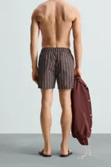 Bañador corto de hombre con estampado de rayas verticales en marrón, blanco y azul. Cuenta con cintura elástica ajustable con cordón, bolsillos laterales y trasero.