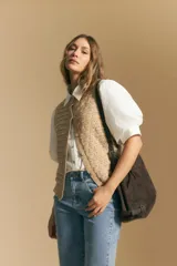 Chaleco tejido sin mangas color blanco roto, con cuello redondo y cartera frontal de botones. Presenta un punto calado con textura.