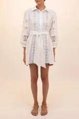 Camisa blanca con cuello clásico, cierre frontal con botones, mangas largas abullonadas con puños elásticos y detalles de encaje en el frente y las mangas. Incluye cinturón de tela.