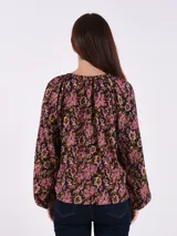 Blusa estampada con flores en tonos rosa, negro y verde. Tiene cuello redondo con abertura en forma de lágrima y mangas largas con puños elásticos.