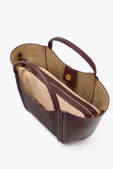 Bolso mini city color borgoña, con asa de mano y asa bandolera extraíble. Tiene detalle de pespuntes en contraste y bolsa interior extraíble con cierre de cremallera.