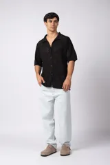 Camisa negra tejida de manga corta, con calado aireado, cuello tipo bowling y botones al tono. Diseño de corte relajado.