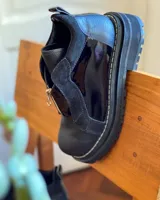 Botines de cuero negro con paneles laterales de charol, cierre frontal con cremallera y suela track.