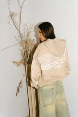 Hoodie con cierre frontal de algodón color crema con lavado acid wash. Presenta un logo estilizado en el pecho y estampados gráficos con caracteres orientales en ambas mangas.