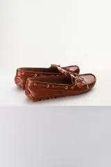 Mocasines plateados de cuero con cordones decorativos y suela de goma marrón.