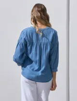 Blusa celeste de lyocell con cuello a la base y escote en V con apertura central y botones. Manga ¾ con puño y botón.