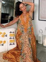 Vestido largo tipo solera, con escote halter profundo y silueta muy holgada. Presenta un estampado vibrante que combina patrón de leopardo en tonos naranjas y marrones con detalles de paisley en tonos azules y turquesas.
