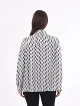 Camisa blanca estampada con motivos geométricos negros, de corte holgado, manga larga y cuello camisero.