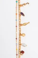 Pulsera dorada de doble cadena con charms colgantes de diferentes formas y colores, incluyendo piedras, perlas y dijes metálicos.