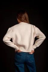 Buzo gris de punto con cuello redondo, mangas largas abullonadas y cierre frontal asimétrico.