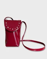 Cartera porta celular roja charolada con correa larga y tapa con broche a presión decorada con tachas plateadas.