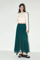 Falda midi verde esmeralda de satén, de tiro alto y corte evasé, con bajo asimétrico y forro interior.