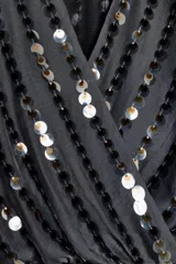 Body negro con escote en V cruzado, mangas largas acampanadas y apliques de lentejuelas.