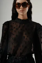 Blusa negra de manga larga con cuello alto y textura transparente con apliques florales en relieve.