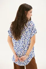 Blusa estampada con hojas azules sobre fondo blanco, con cuello en V y mangas cortas con dobladillo.