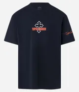 Remera negra de algodón con corte relaxed, cuello redondo y mangas cortas. Estampa frontal con una cruz y el nombre "Tupac Shakur" en color naranja.