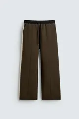 Pantalón jogger color verde oliva, corte relaxed fit, con cintura elástica ajustable con cordón, bolsillos laterales y detalle de bolsillo de vivo en la espalda. Presenta una banda lateral color crema a contraste.